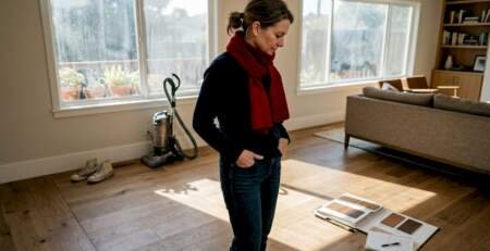 Homeowner inspects hardwood floors in sunlit Bay Area living room